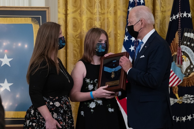 A man gives a framed medal to two women.