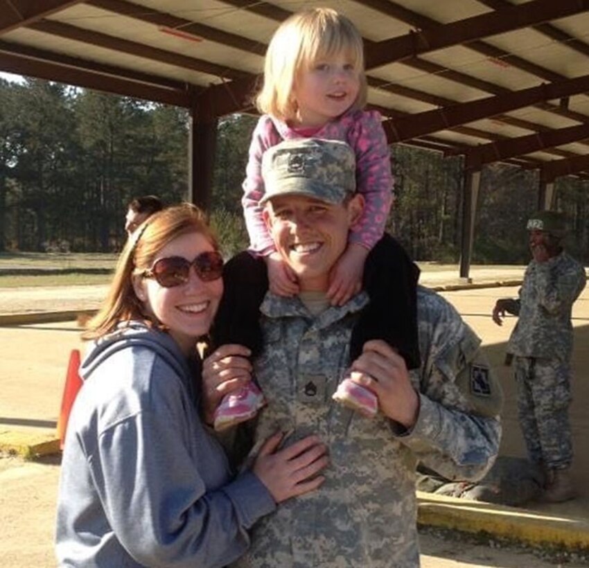 A woman hugs a man who has a child on his neck; the three are smiling.