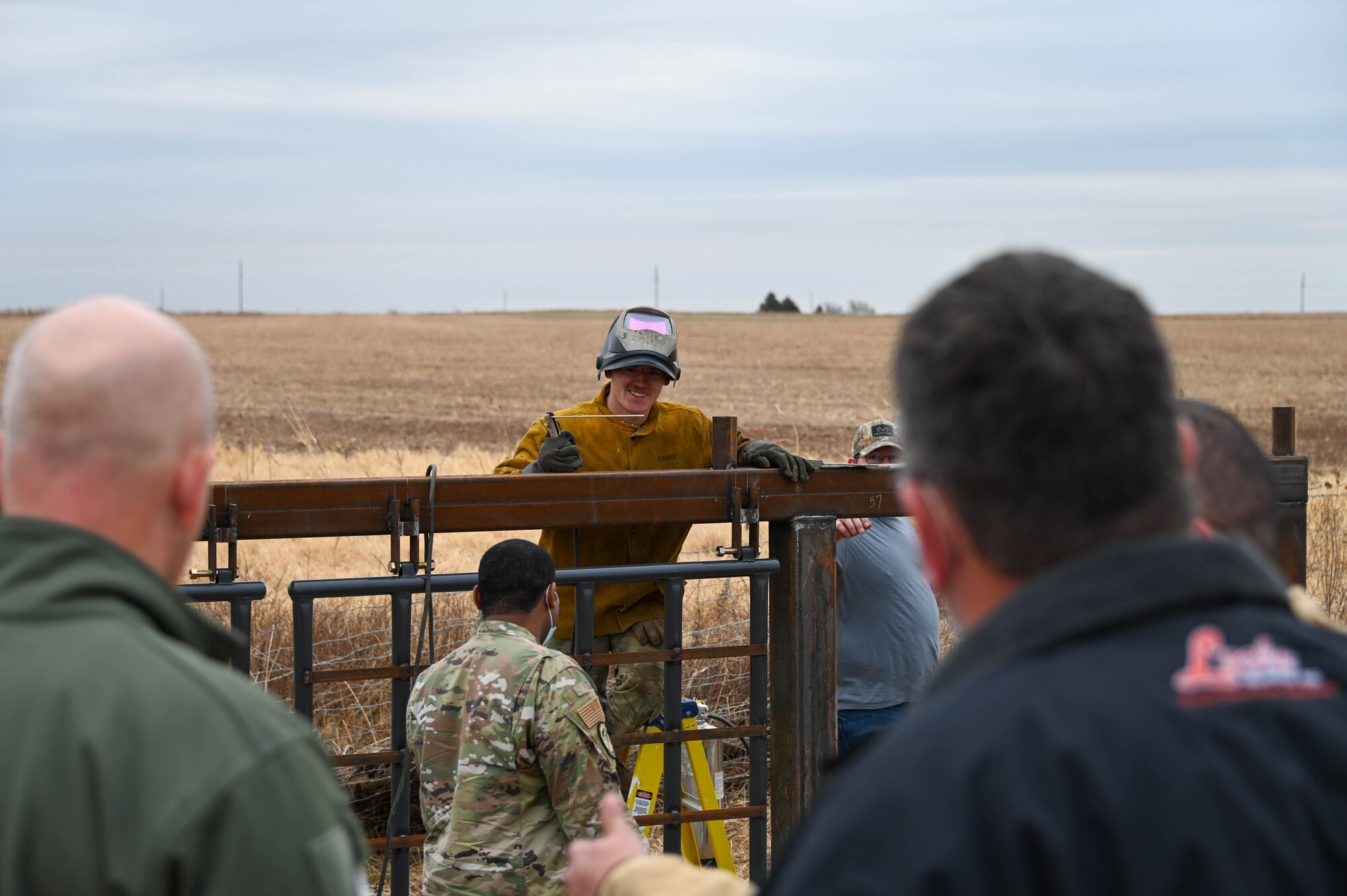 U.S. Air Force Senior Airman James Gonzales, 97th Civil Engineering Squadron equipment operator, and Chief Master Sergeant Ceasar Flores, 97th Air Mobility Wing command chief, pose for a photo at Altus Air Force Base, Oklahoma, Dec. 17, 2021. Flores helped Gonzales remove a pin from a fence with the rock he is holding. (U.S. Air Force photo by Airman 1st Class Kayla Christenson)