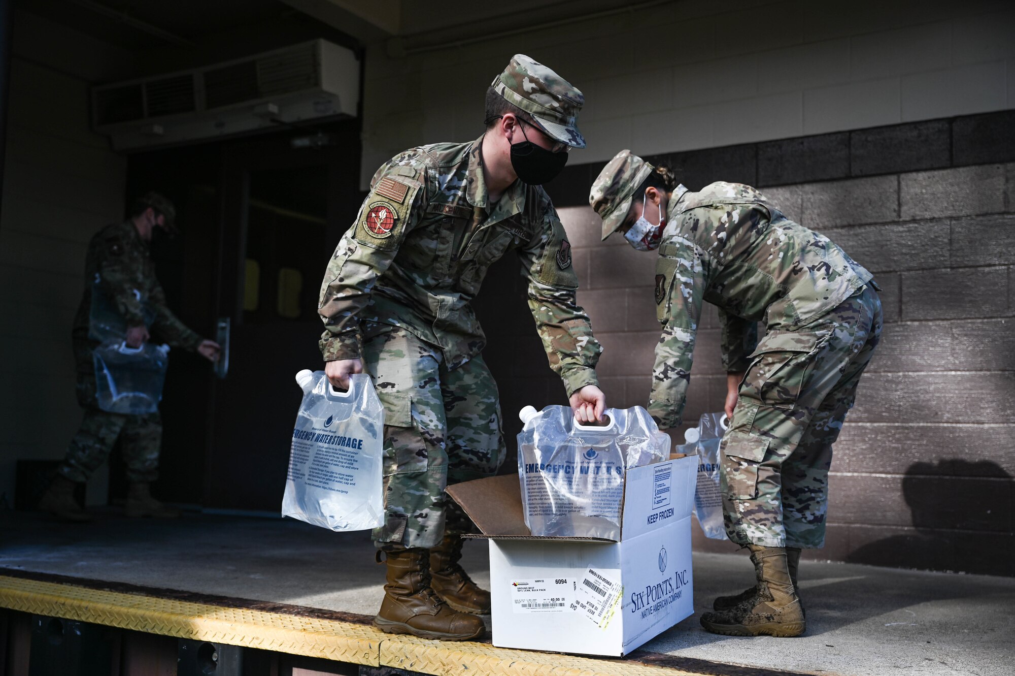 Staff Sgt. Sarah Sanez, 647th Force Support Squadron food service supervisor, Airman 1st Class Jacob MacKenzie and Senior Airman Joseph McCabe, 647th FSS food service journeymen, transport potable water into the Hale Aina Dining Facility at Joint Base Pearl Harbor-Hickam, Hawaii, Dec. 16, 2021. An estimated 80 gallons of potable water is used per day at the facility as a precautionary measure. Night-shift food service personnel are responsible for refilling all water containers before the end of their shift, ensuring the day-shift personnel are readily available to cook on arrival the following day. (U.S. Air Force photo by Staff Sgt. Alan Ricker)