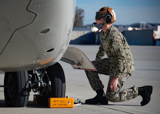 Aviation Electrician’s Mate 2nd Class Sean Moran, assigned to the “Sunhawks” of VRM 50, places chocks on the landing gear of a CMV-22B Osprey on the flight line on board Naval Air Station North Island. (U.S. Navy/ MC2 Chelsea D. Meiller)