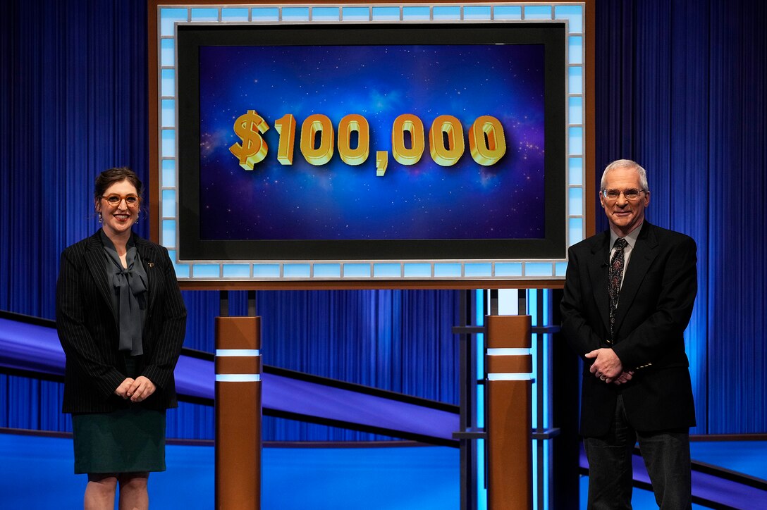 Two people stand by a screen that says $100,000
