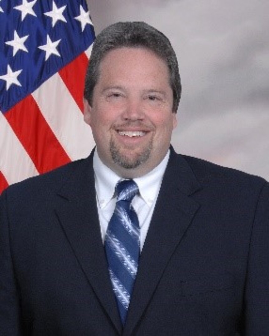 man in dark suit with American flag in the background
