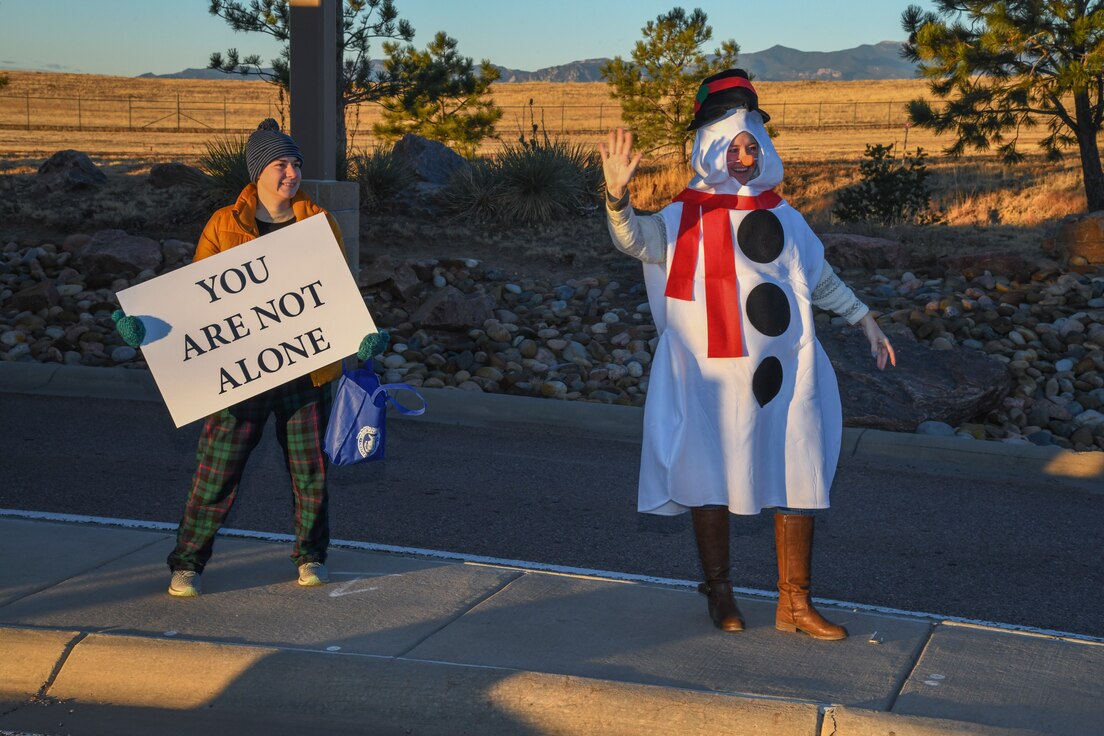 U.S. Air Force Capt. Lindsey Moser, Peterson-Schriever Garrison chaplain holds and sign while U.S. Ai Force Tech. Sgt. Lathaniel Leigh, P-S GAR religious affairs noncommissioned officer in charge, greets incoming cars at the Enoch gate on Schriever Space Force Base, Dec. 17, 2021.