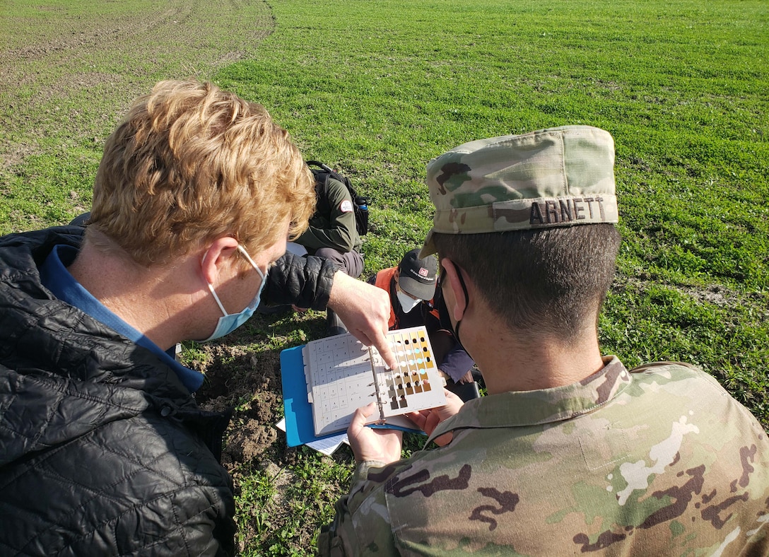 two white males look down at a book over a field