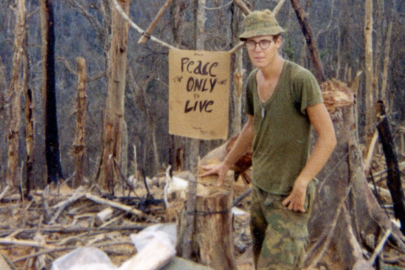 A young Marine stands next to a large peace sign and poses for a photo.