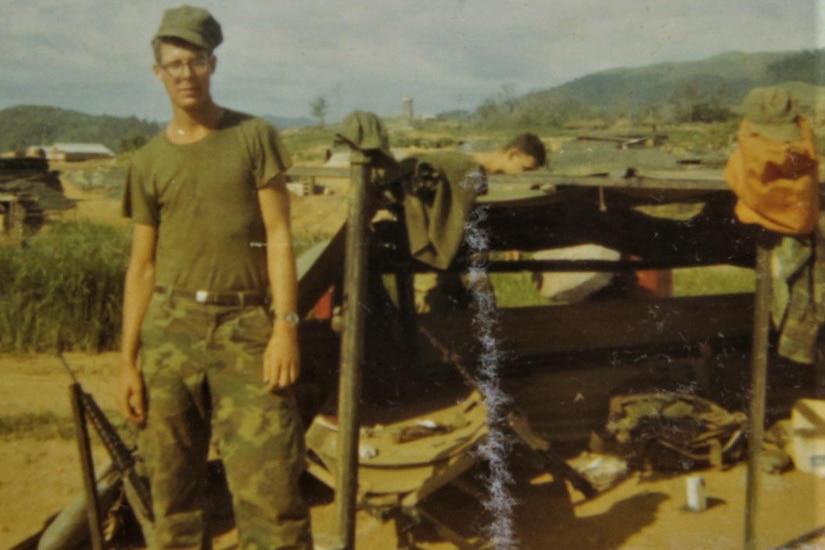 A Marine stands next to a tent looking at a camera.