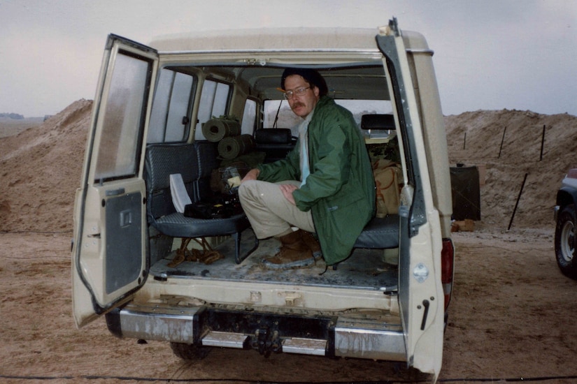 A man sits in the back of a vehicle with the doors open and poses for a photo.