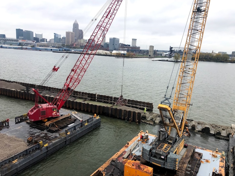 Cranes construct a breakwater with metal sheetpile walls in a harbor.