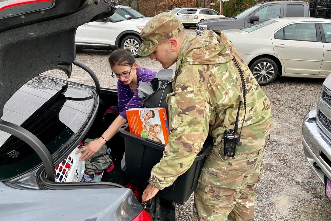 A soldier helps a resident place supplies in the trunk of a car.