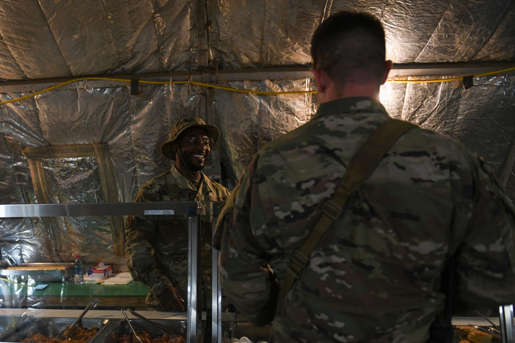 U.S. Air Force Staff Sgt. Anthony Guinn, 776th Expeditionary Air Base Squadron food services supervisor, smiles while he serves food at Chabelley Airfield, Djibouti, Dec. 8, 2021. Guinn strives to make people laugh and smile as he works because he believes everything he does starts with the people. (U.S. Air Force photo by Senior Airman Ericka A. Woolever)