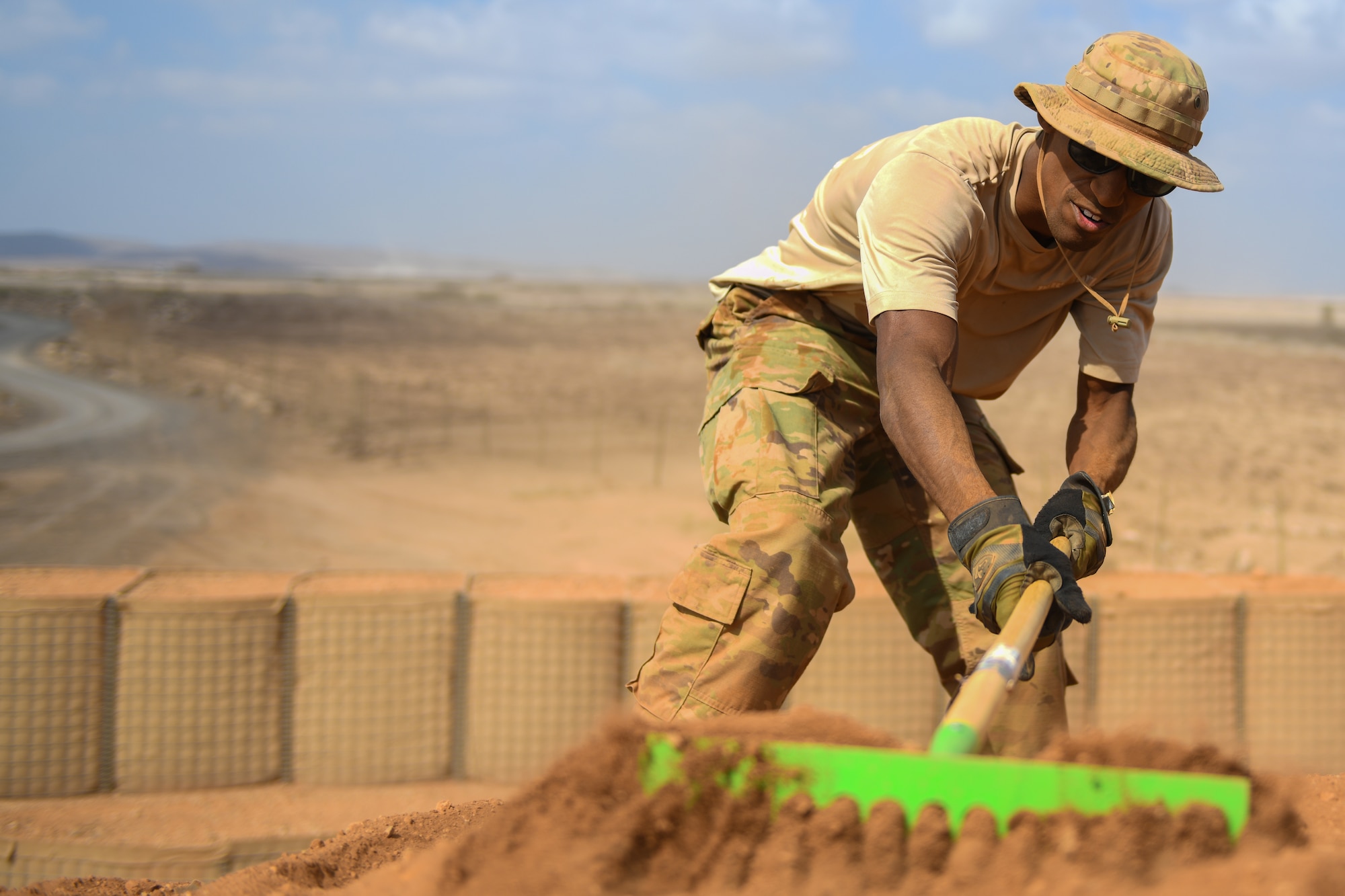 U.S. Air Force Senior Airman Erek Bowens, 776th Expeditionary Air Base Squadron heavy equipment operator, rakes dirt to level out the ground of a storage area at Chabelley Airfield, Djibouti, Dec. 8, 2021. Bowen’s mission at Chabelley Airfield is to support base infrastructure while also ensuring an operational airfield. (U.S. Air Force photo by Senior Airman Ericka A. Woolever)