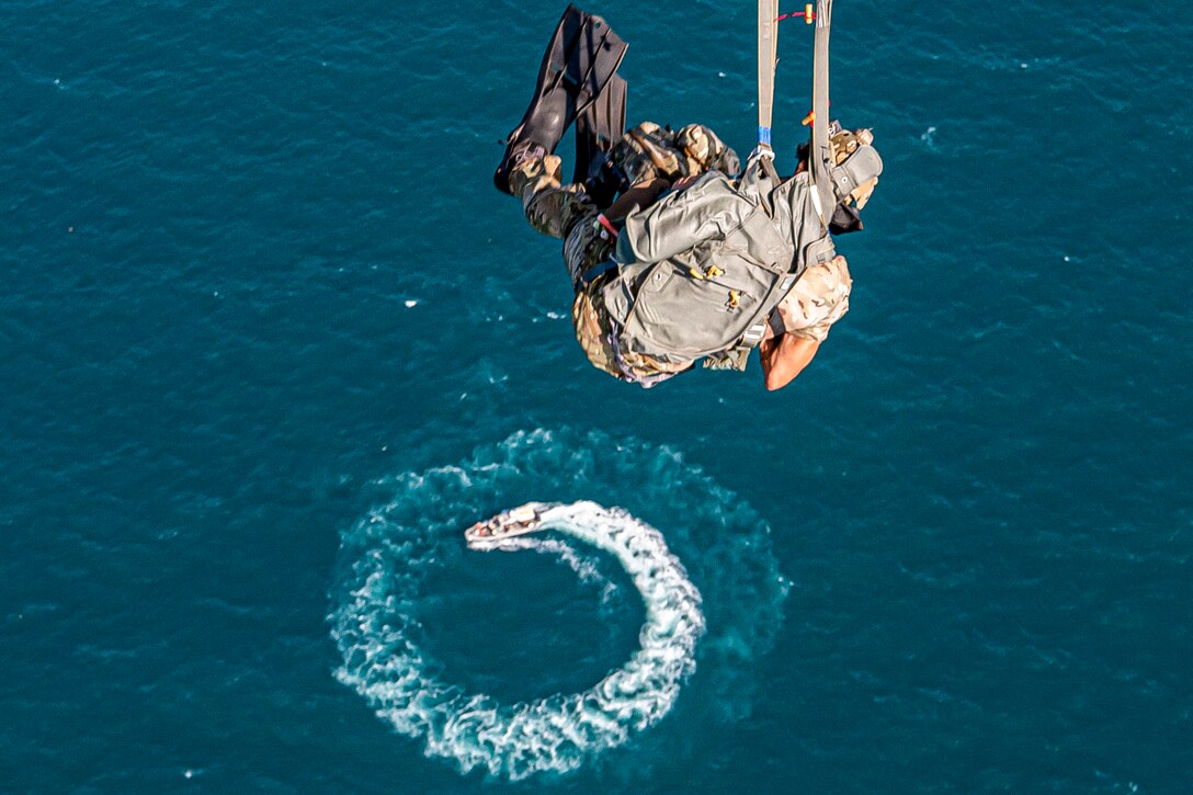 An airman wearing flippers descends as a boat circles below.