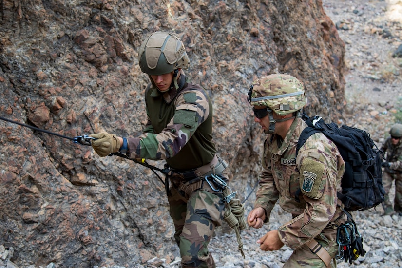 U.S. Army Staff Sgt. Elijah Amendola, 1-102nd Infantry Regiment (Mountain), Task Force Iron Gray, Combined Joint Task Force – Horn of Africa (CJTF-HOA), assists a French service member with the 5th Overseas Interarms Regiment (5e RIAOM) on fixed rope techniques at the Arta Range Complex, Djibouti, Dec. 15, 2021. Five instructors from the U.S. Army Mountain Warfare School in Jericho, Vermont, taught a five-day Joint Expeditionary Mountain Warfare Course on basic military mountaineering skills to French service members in Djibouti to strengthen the relationships among the international forces working together in the region.