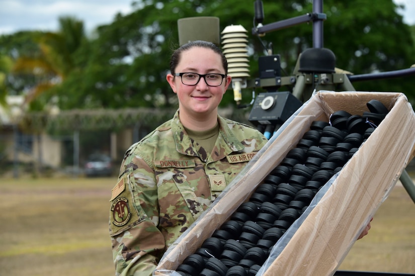 An airman stands outside with a box of shoes.