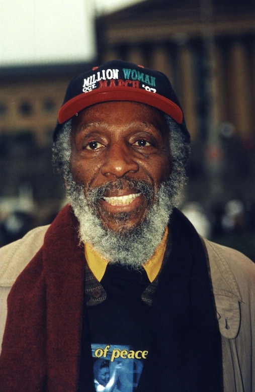 A man smiles for a photo while wearing a Million Women March baseball cap.