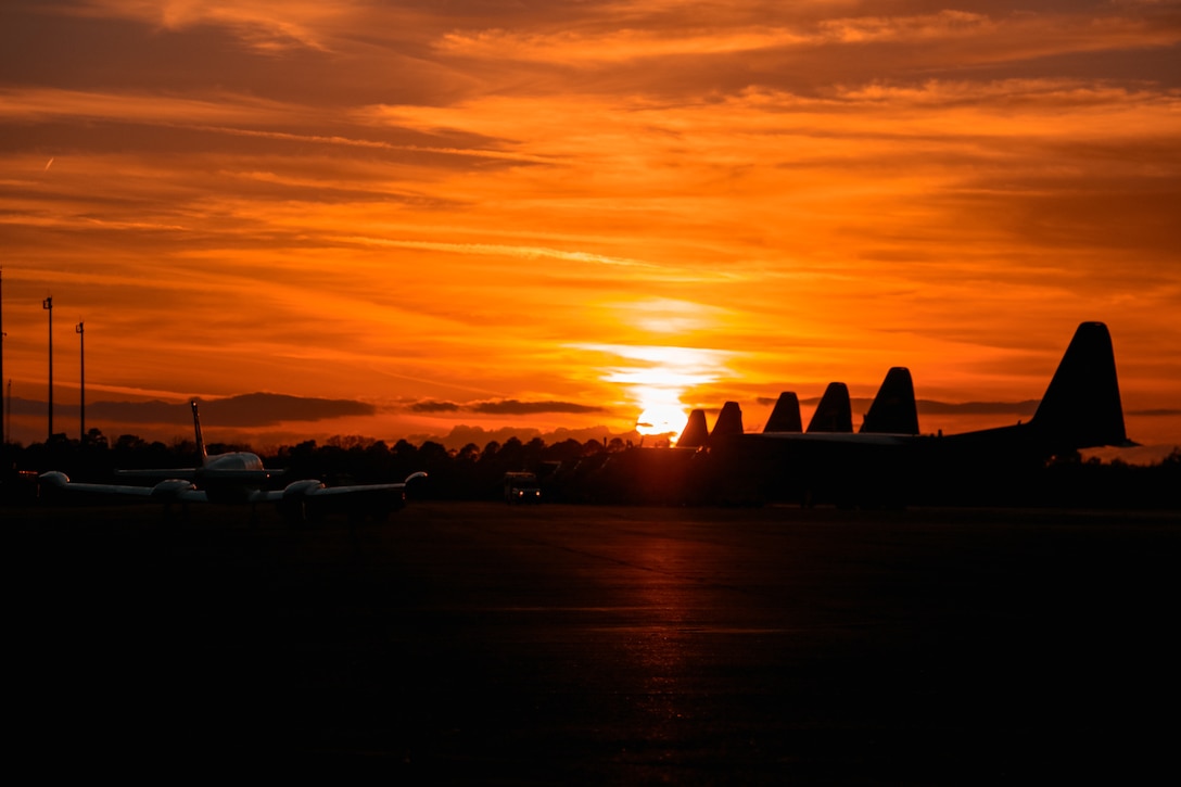 Six aircraft sit in silhouette on a flightline with a golden sky in the background.