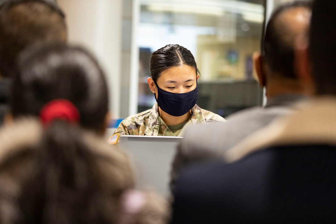 A soldier sits at a table while checking in guests.