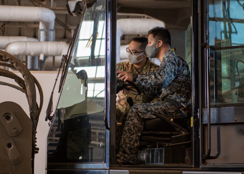 A U.S. Air Force Airman explains the controls of a 10K All-terrain Forklift to a member of the Japan Air Self Defense Force.