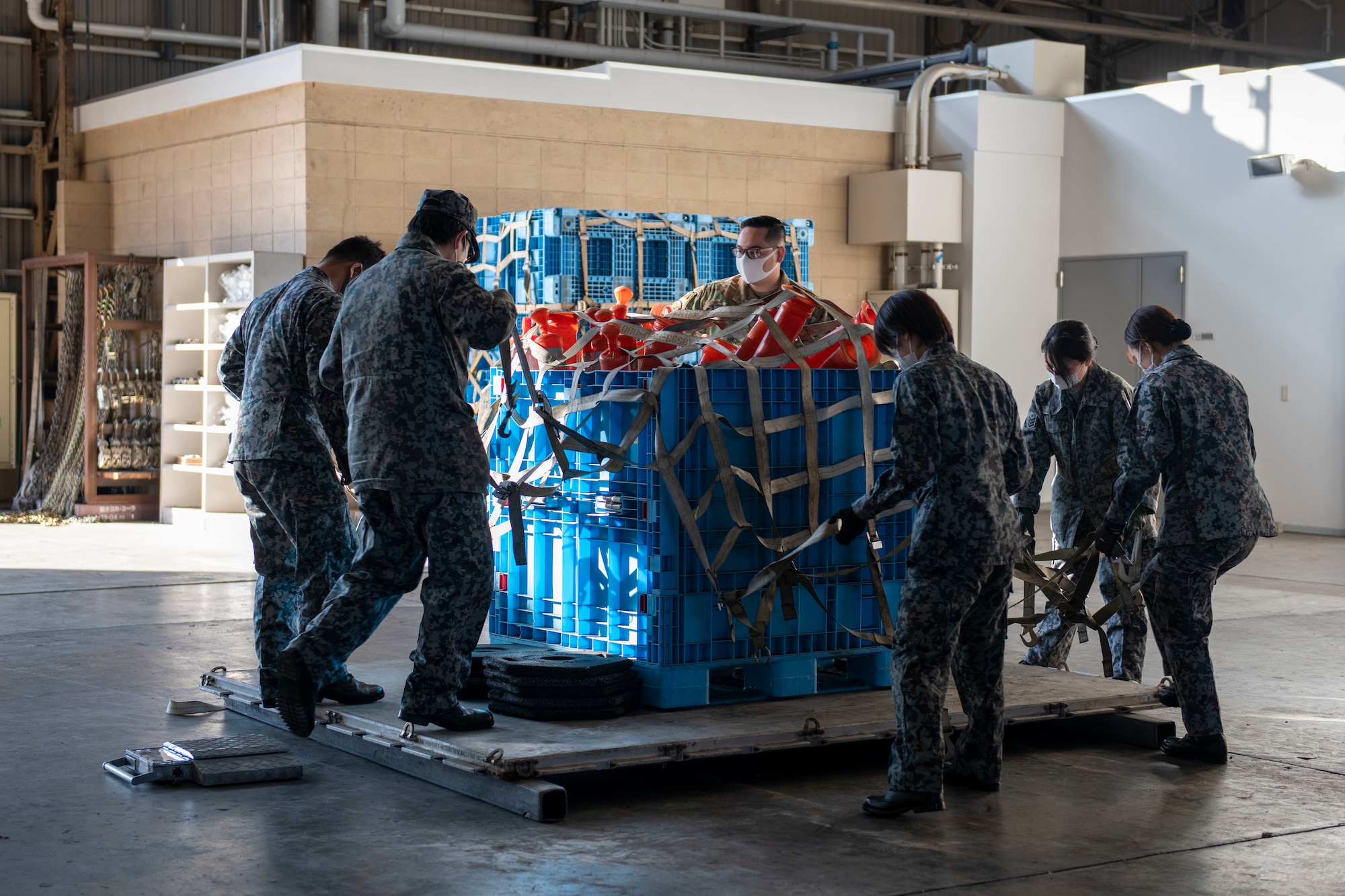 A U.S. Air Force Airman and members of the Japan Air Self Defense Force place a cargo net over a loaded shipping pallet