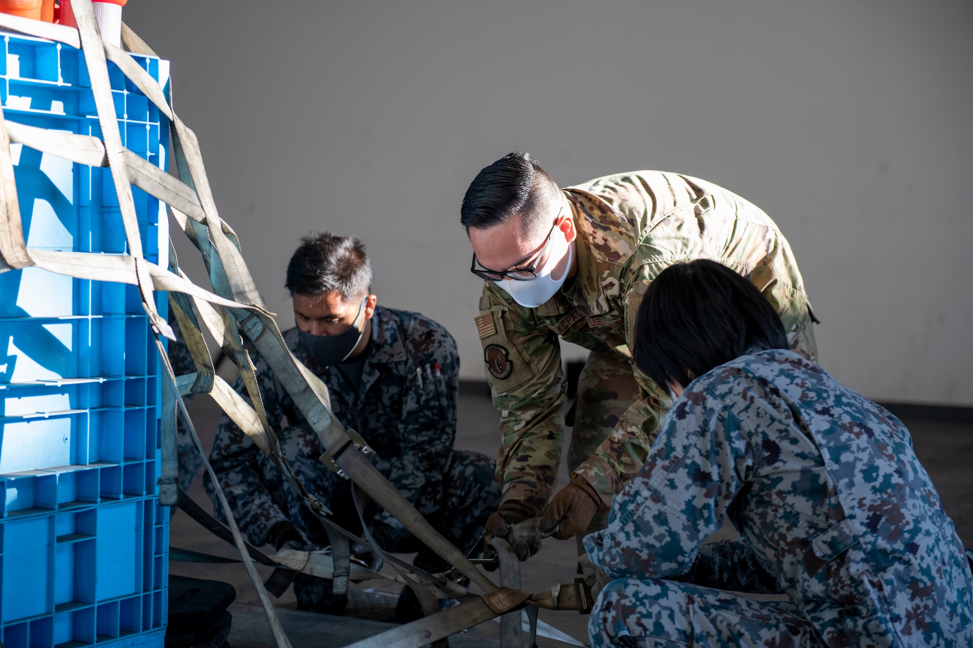 A U.S. Air Force Airman and members of the Japan Air Self Defense Force secure cargo onto a pallet using cargo nets.