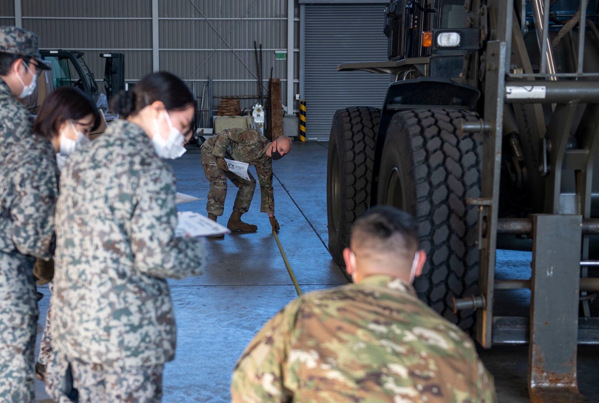 A U.S. Air Force Airman measures the length of 10K All-Terrain Forklift alongside members of the Japan Air Self Defense Force