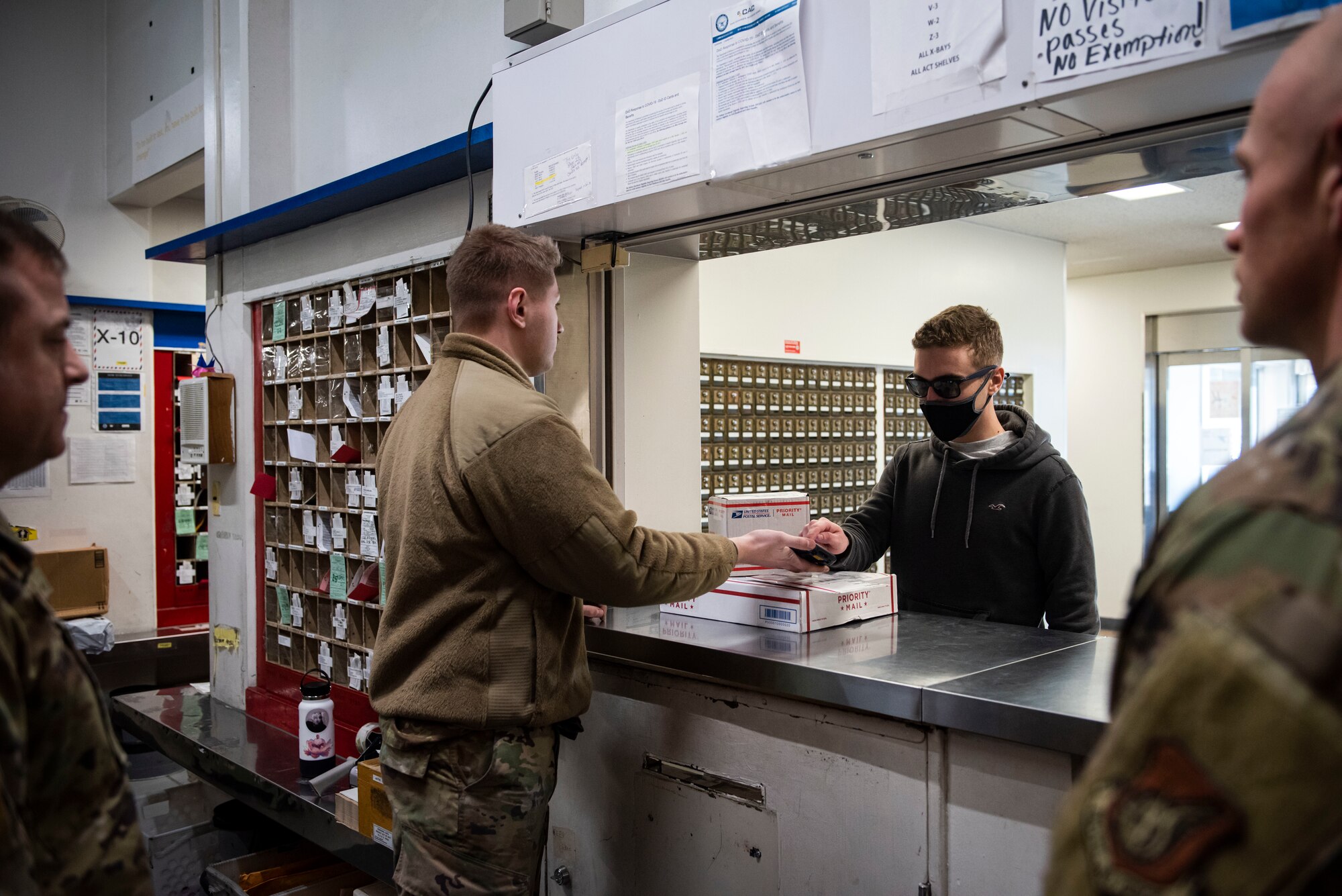 Military members in uniform hands out mail to customers through the Post Office window.