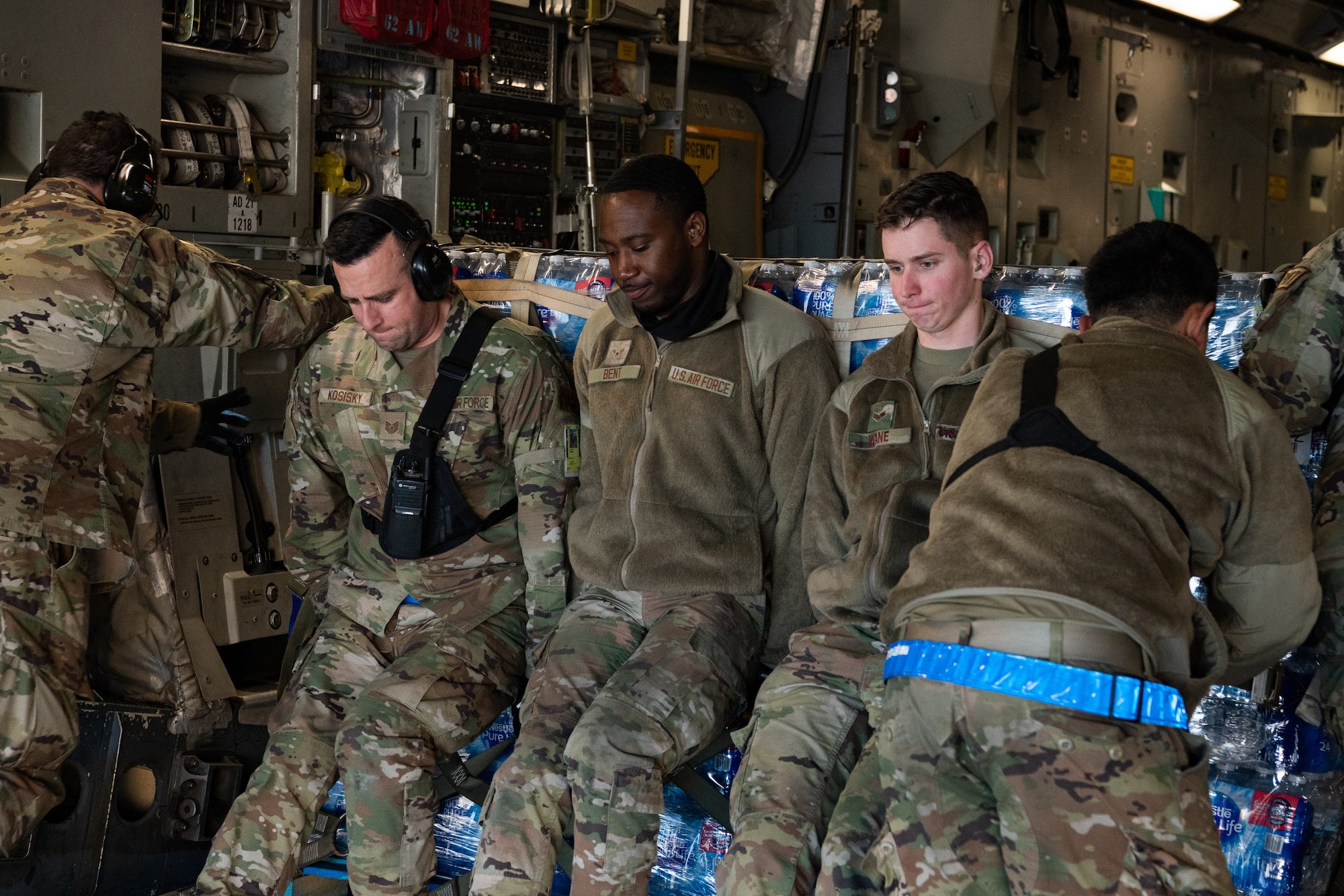 Six Airmen push a pallet filled with water onto an aircraft.