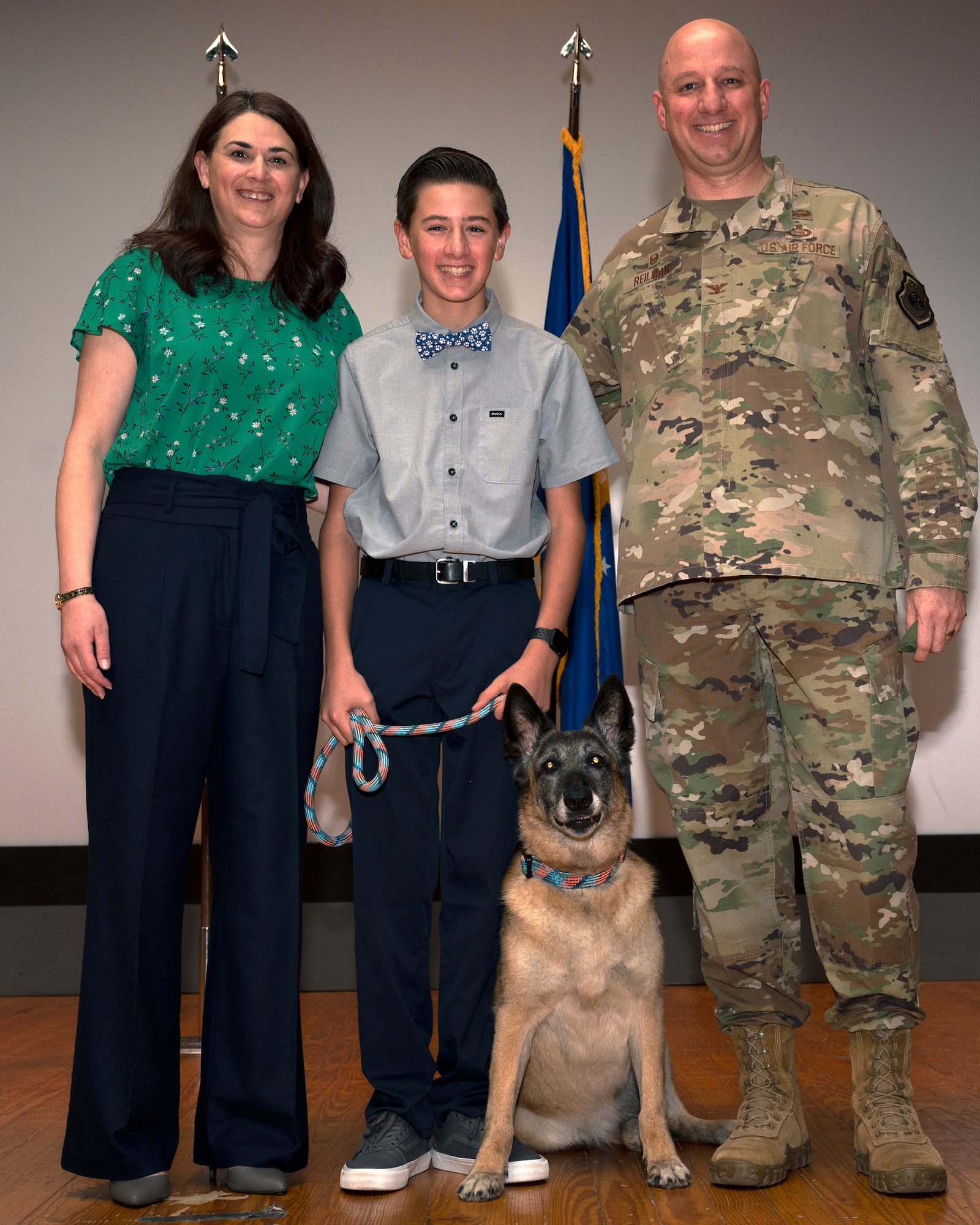 The Reilman family poses for a photo with 17th Security Forces Squadron Military Working Dog Joy during her retirement ceremony at the theater on Goodfellow Air Force Base, Dec. 20. The Reilman family has adopted Joy, giving her a home on the base she served as she transitions into retirement. (U.S. Air Force photo by Senior Airman Michael Bowman)