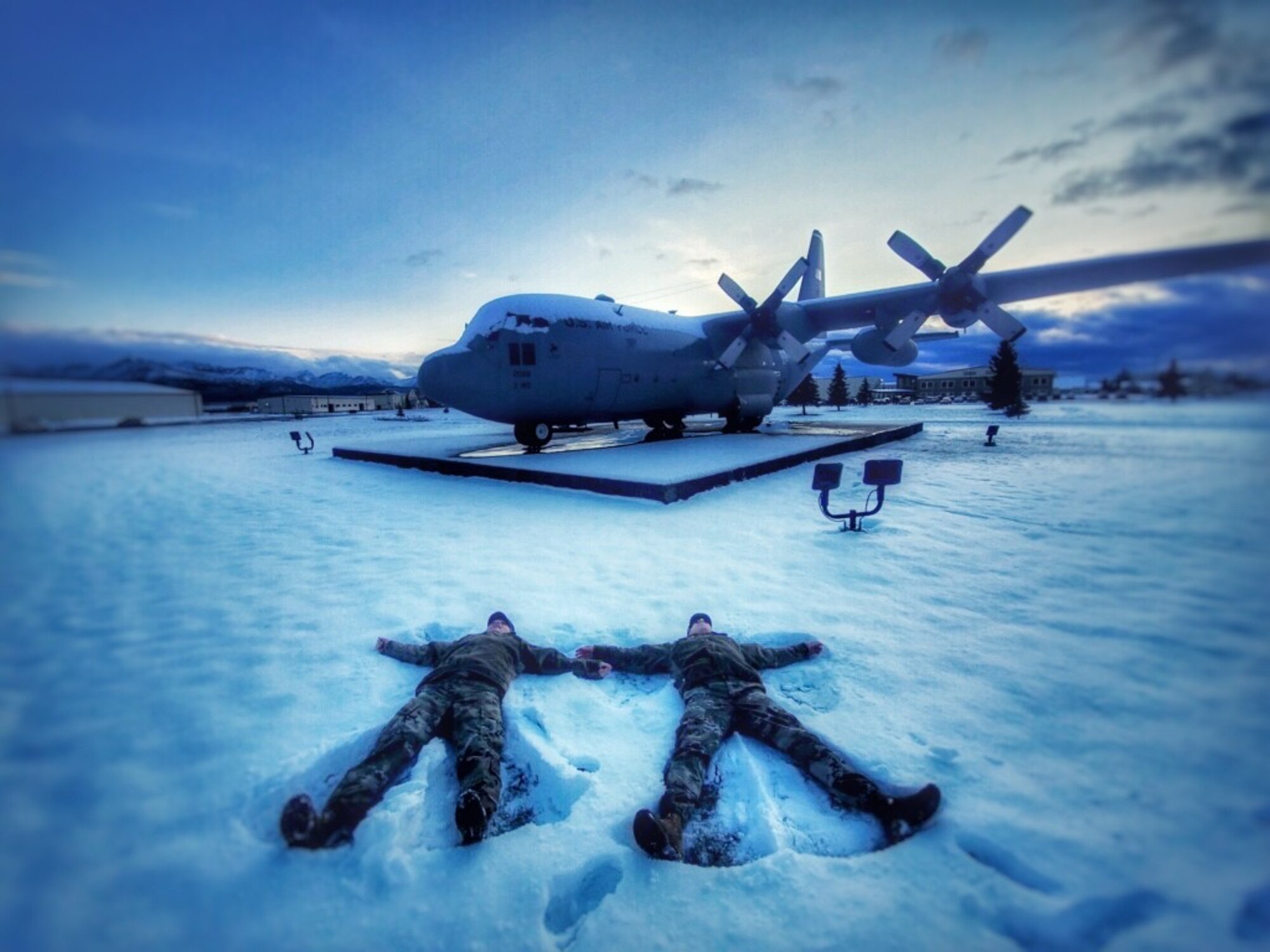 Two individuals lay in the snow and make "snow angels."