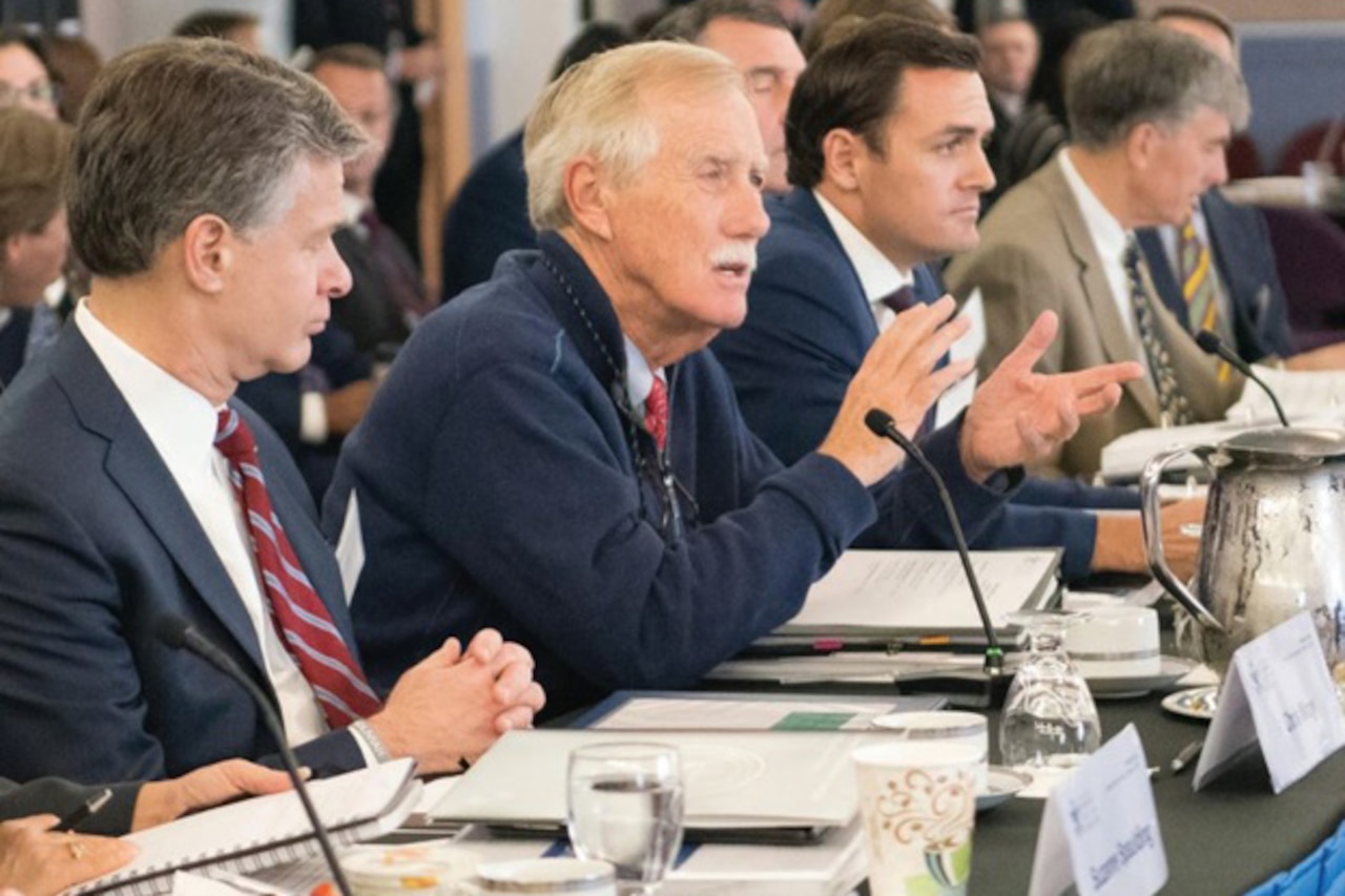 A man speaks alongside others in a panel table.