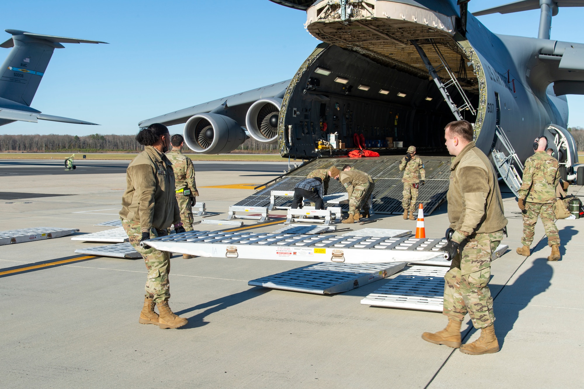 Ramp services personnel from the 436th Aerial Port Squadron place a modular ramp system in position to facilitate the loading of water filtration equipment to a C-5M Super Galaxy at Dover Air Force Base, Delaware, Dec. 20, 2021. An aircrew from the 9th Airlift Squadron flew the equipment to Joint Base Pearl Harbor-Hickam (JBPHH), Hawaii. The JBPHH water quality recovery is a joint U.S. military initiative working closely with the State of Hawaii, Department of Health, Honolulu Board of Water Supply, U.S. government and independent organizations to restore a safe water delivery system to JBPHH military housing communities through testing, treatment, and repair. For detailed information, including available resources and locations, and news, go to www.navy.mil/jointbasewater.   (U.S. Air Force photo by Roland Balik)(This photo has been altered for security purposes by blurring out identification badges.)