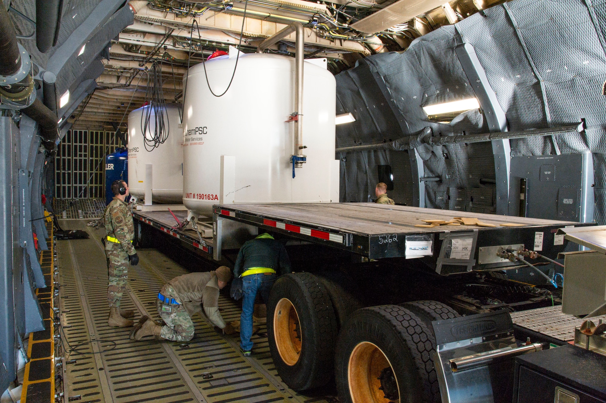 A 436th Aerial Port Squadron ramp services load team secures a trailer loaded with water filtration equipment at Dover Air Force Base, Delaware, Dec. 20, 2021. A C-5M Super Galaxy aircrew assigned to the 9th Airlift Squadron, flew the equipment to Joint Base Pearl Harbor-Hickam (JBPHH), Hawaii. The JBPHH water quality recovery is a joint U.S. military initiative working closely with the State of Hawaii, Department of Health, Honolulu Board of Water Supply, U.S. government and independent organizations to restore a safe water delivery system to JBPHH military housing communities through testing, treatment, and repair. For detailed information, including available resources and locations, and news, go to www.navy.mil/jointbasewater.   (U.S. Air Force photo by Roland Balik) (This photo has been altered for security purposes by blurring out identification badges.)