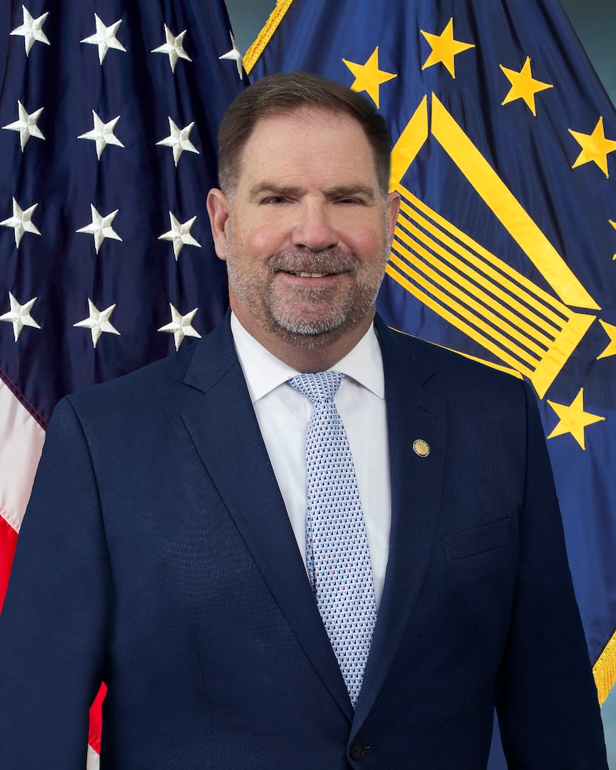 Mike Cannon in blue suit in front of American flag and the SES flag