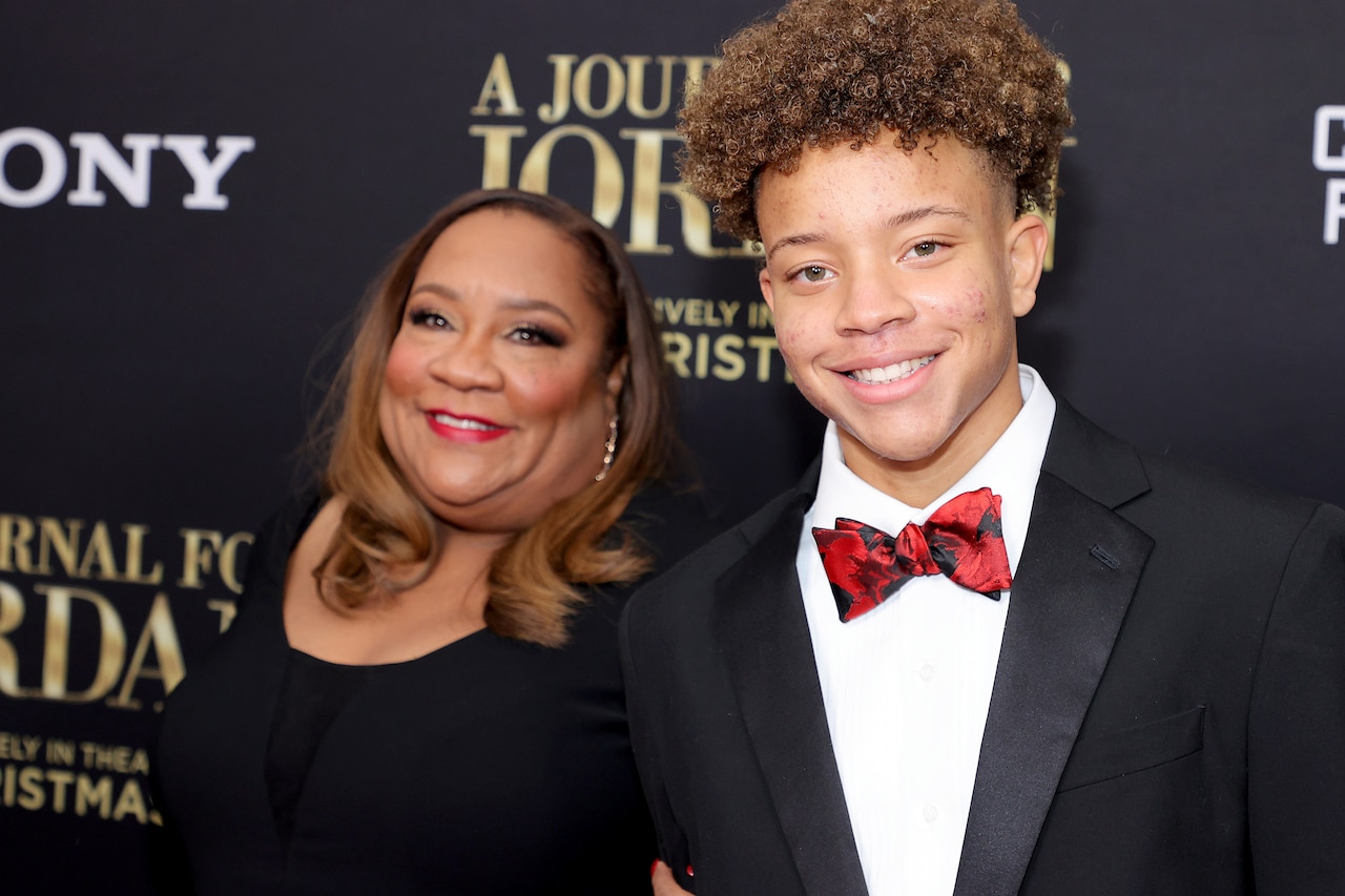 A woman stands near a teenage male who wears a tuxedo.