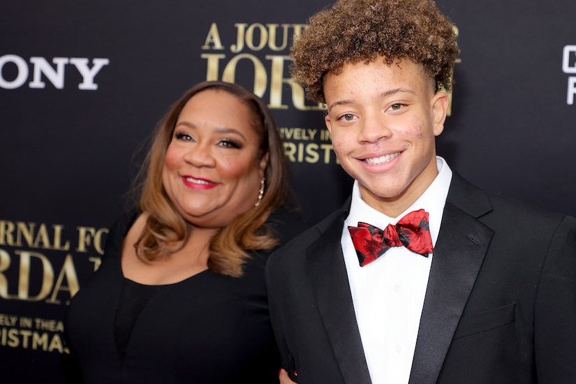 A woman stands near a teenage male who wears a tuxedo.