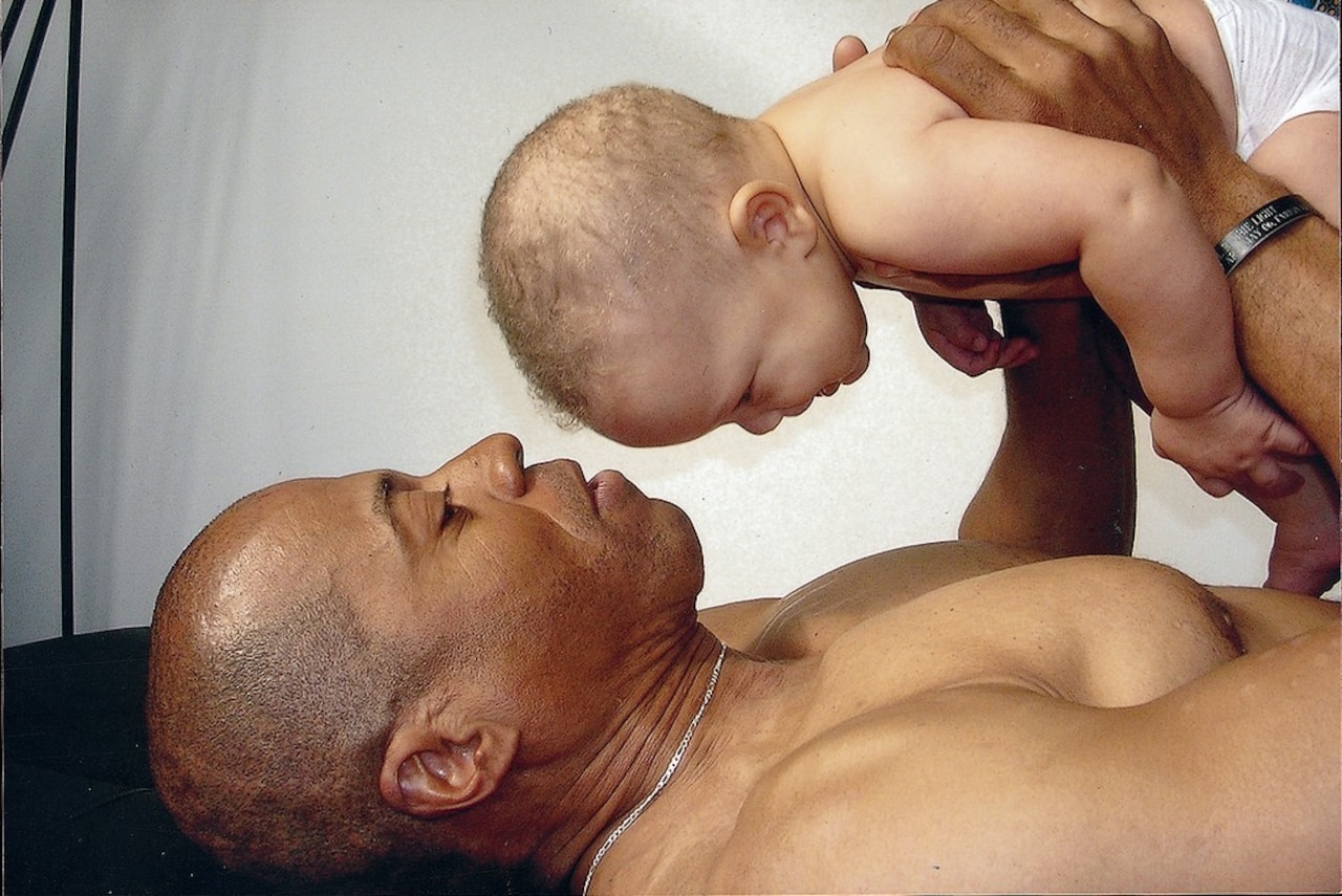 A man lies on his back. He holds an infant above him.
