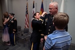 Chief Warrant Officer 5 Brian Brooks looks on as Chief Warrant Officer 5 Teresa Domeier, the command chief warrant officer of the Army National Guard, and his son, Noah, pin his rank to his uniform while his wife, Chief Warrant Officer 5 Shelly Brooks, has her rank pinned on by their daughter, Amber, during a ceremony at the Herbert R. Temple Army National Guard Readiness Center, Arlington Hall Station in Arlington, Virginia, Dec. 21, 2021. The ceremony represented a rare moment where a married couple were together promoted to chief warrant officer 5 – the top warrant officer rank.