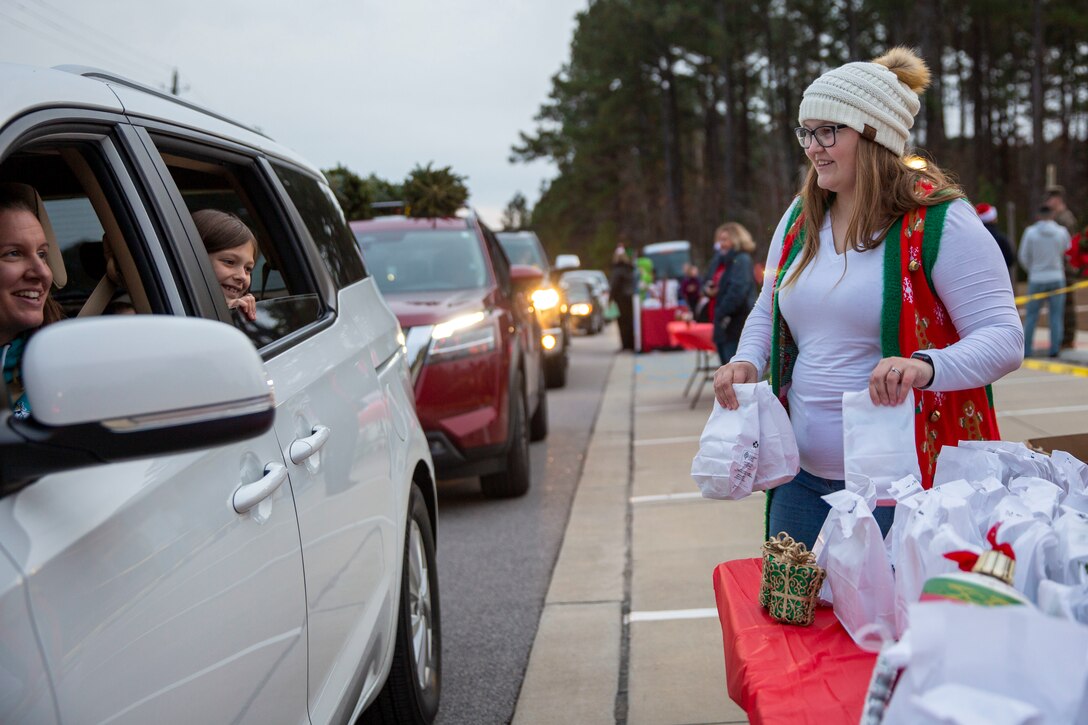 Megan Stewart, an event volunteer, greets service members and their families during the Home for the Holidays drive-thru event at the Knox Community Center on Marine Corps Base Camp Lejeune, North Carolina, Dec. 9, 2021.
