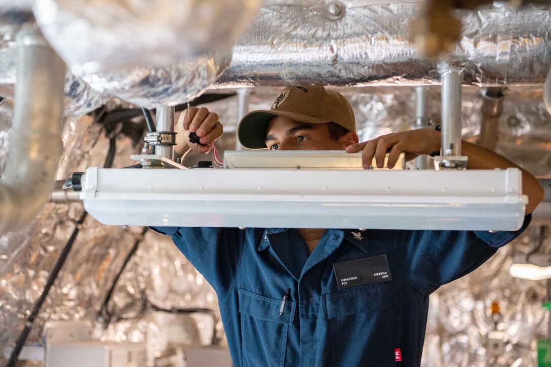 A sailor works on wiring on a light fixture.