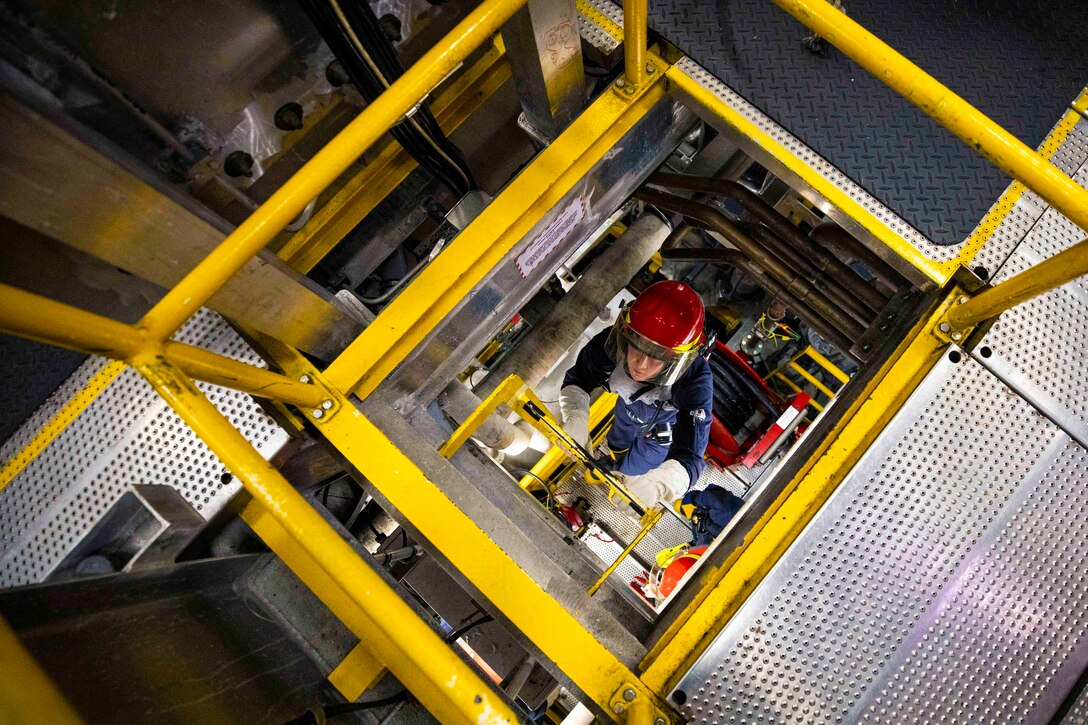 A sailor climbs a ladder while wearing fire protection gear.