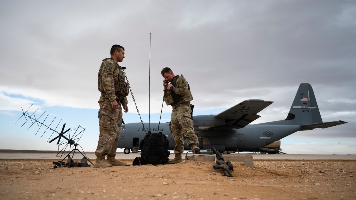 Two soldiers use a communications device near a C-130J super hercules.
