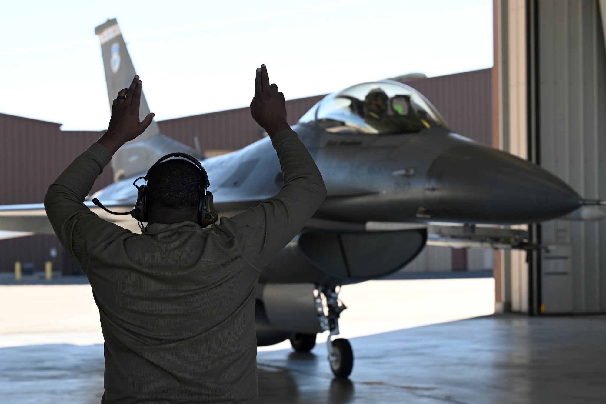 A U.S. Air Force crew chief, assigned to the 8th Aircraft Maintenance Unit, marshals an F-16 Viper to park during a transition ceremony, Dec. 22, 2021, on Holloman Air Force Base, New Mexico. The ceremony culminated with civilian contractors conducting a final departure for an F-16, with enlisted Airmen recovering the aircraft upon return. (U.S. Air Force photo by Staff Sgt. Christopher S. Sparks)