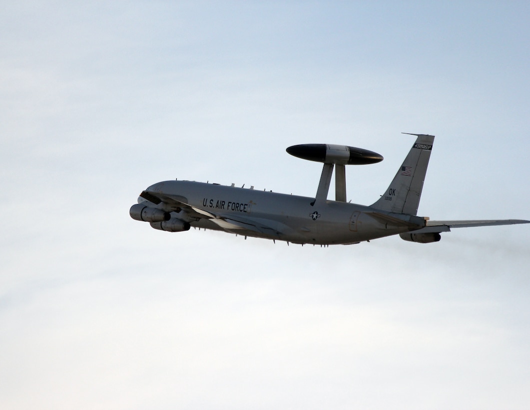 An E-3 Sentry flies in front of a pale blue sky.