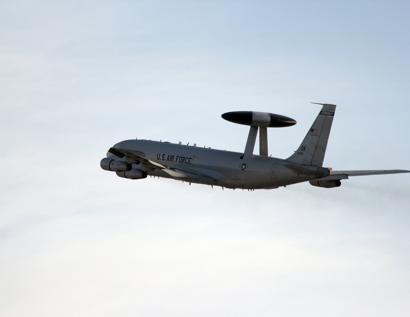 An E-3 Sentry flies in front of a pale blue sky.