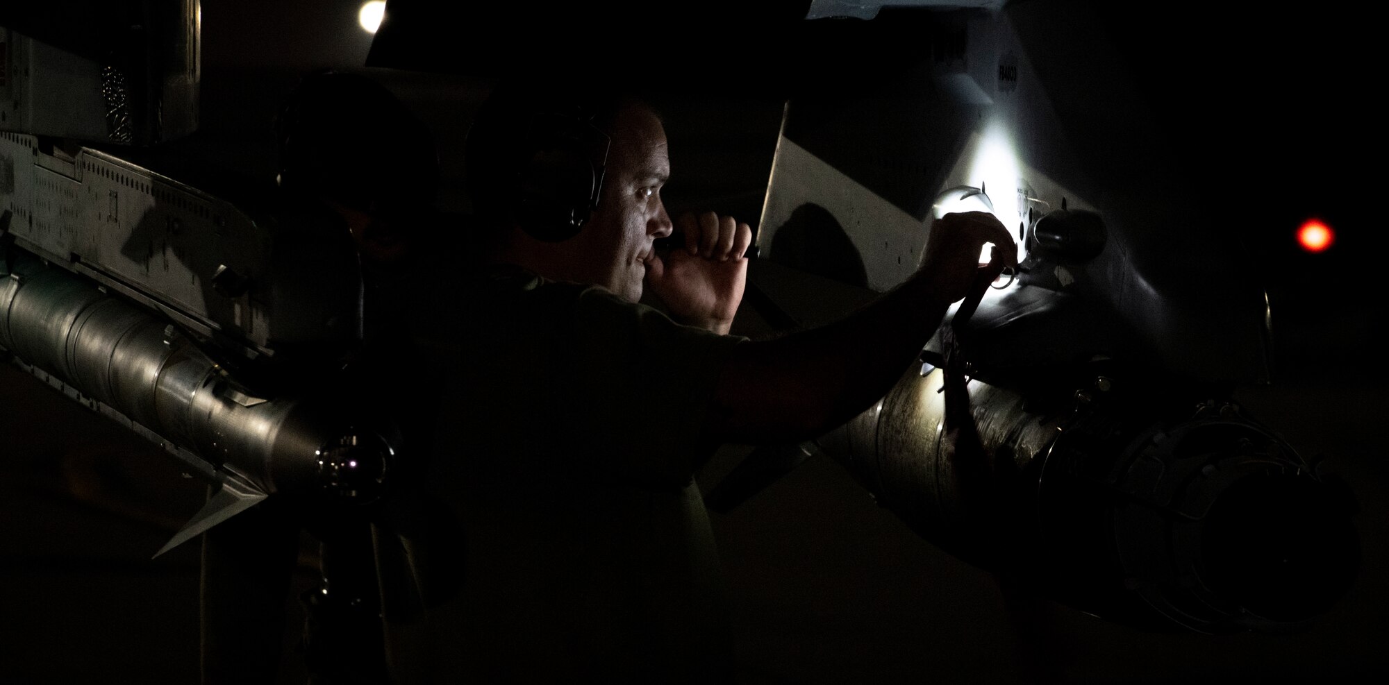Military member looks at aircraft under a flashlight at night.