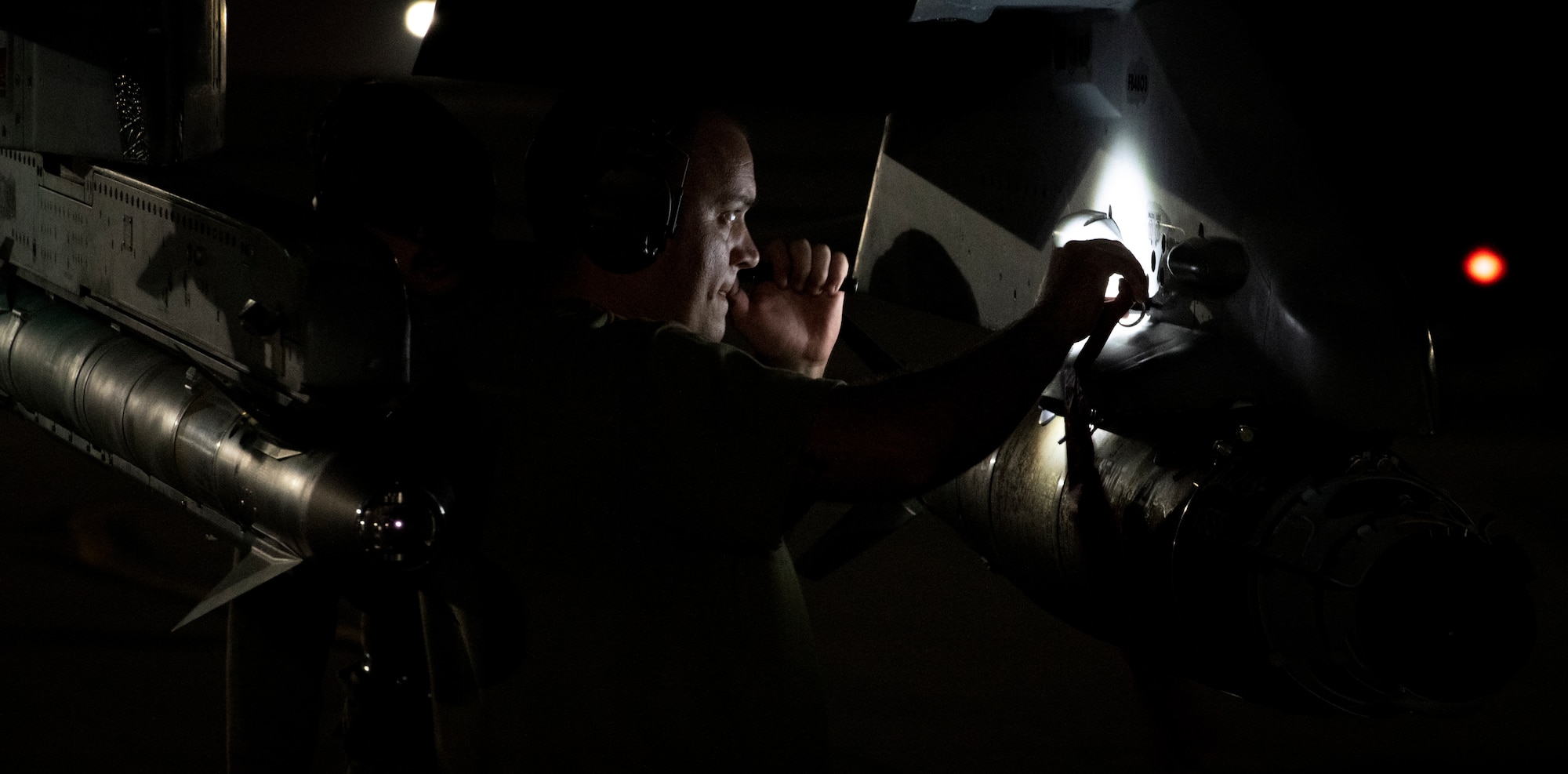 Military member looks at aircraft under a flashlight at night.