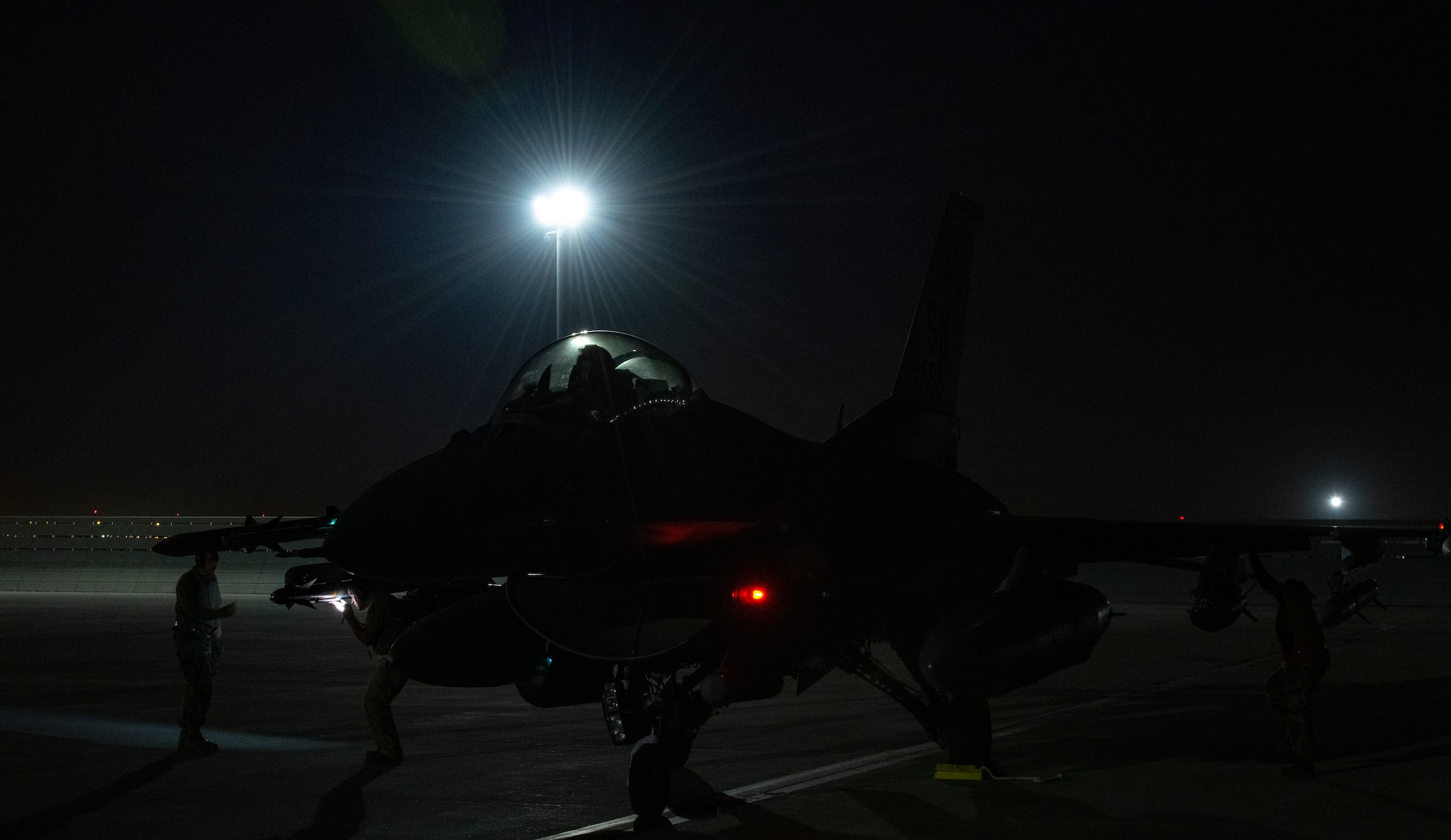 Military jet sits on a flight line at night.