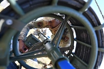 A cyber technician kneels behind a high frequency whip antenna