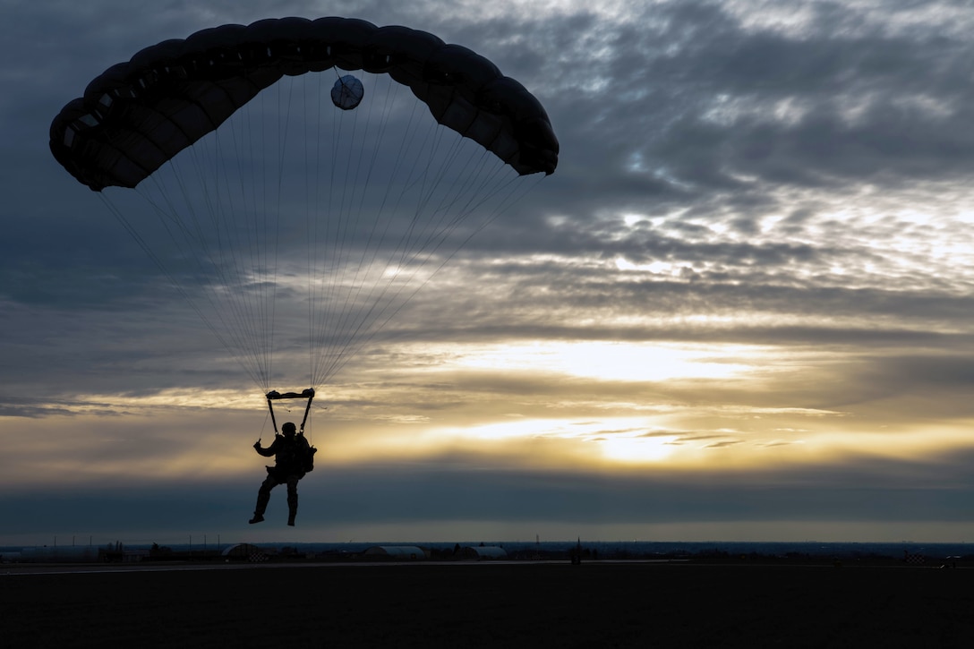 An airman parachutes to the ground at twilight.